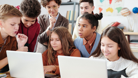 Schulkinder, die sich im Klassenzimmer vor zwei Laptops versammeln